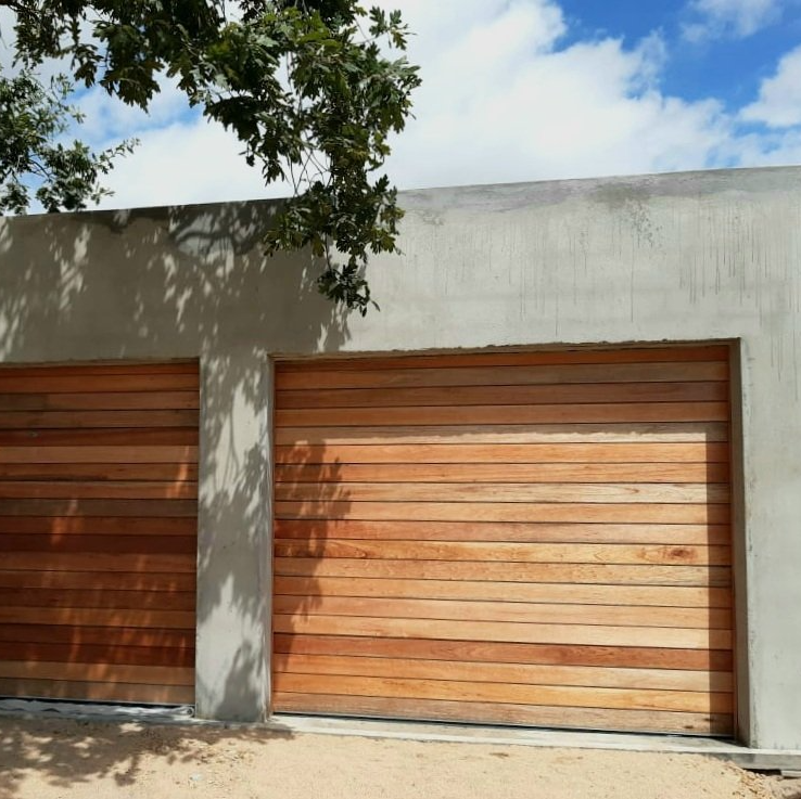 Two wooden garage doors set in a concrete wall, with tree branch overhead and blue sky.