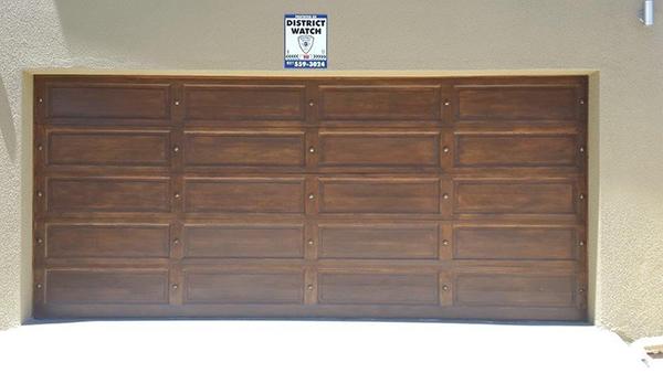 Brown paneled garage door under a security sign, set in a tan wall.
