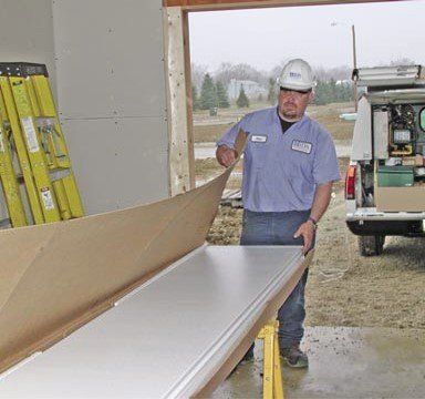 Construction worker in a hard hat removing a white panel from a cardboard box at a building site.