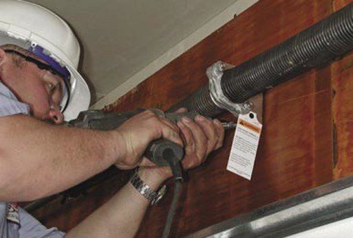 Person in a hard hat using a tool to work on a garage door spring.