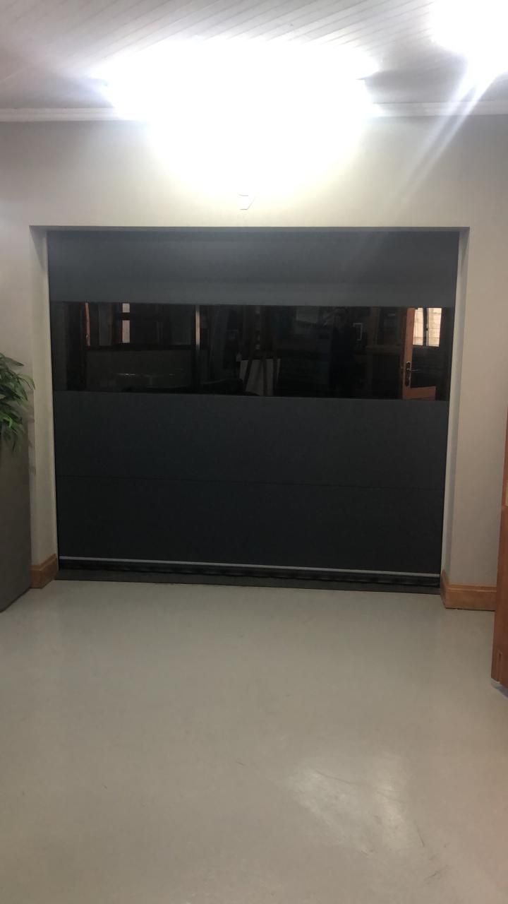 Dark roller shades covering a window in a light-colored room, with a hint of the outdoors visible above.
