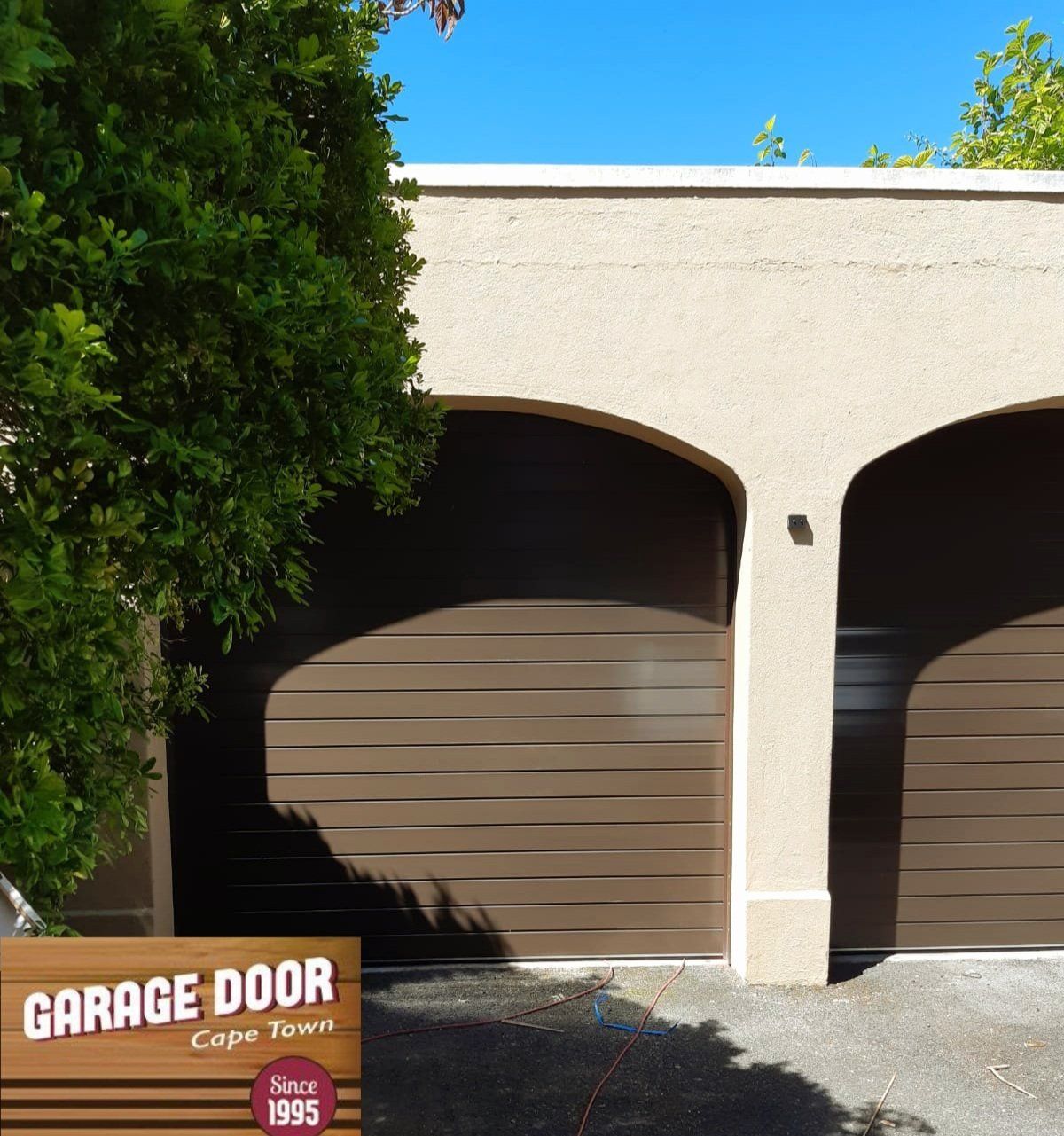 Brown garage doors with arched openings, tan stucco exterior, and a green tree.