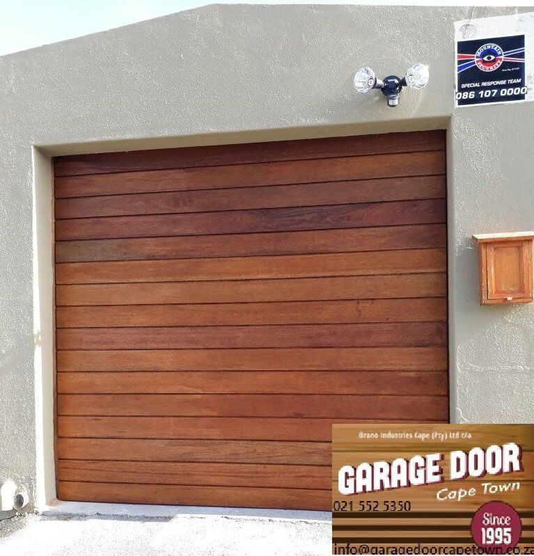 Wooden garage door with horizontal planks on a light-colored building. A security sign and light fixture are above the door.