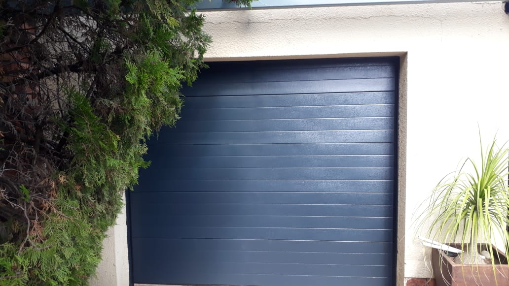 Dark blue garage door, partially obscured by green foliage on the left and potted plants on the right.