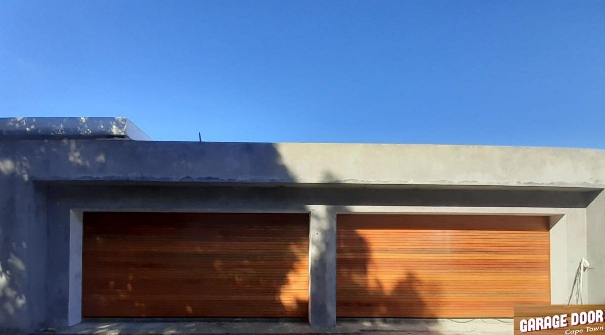 Two wooden garage doors in a concrete building, bright blue sky.