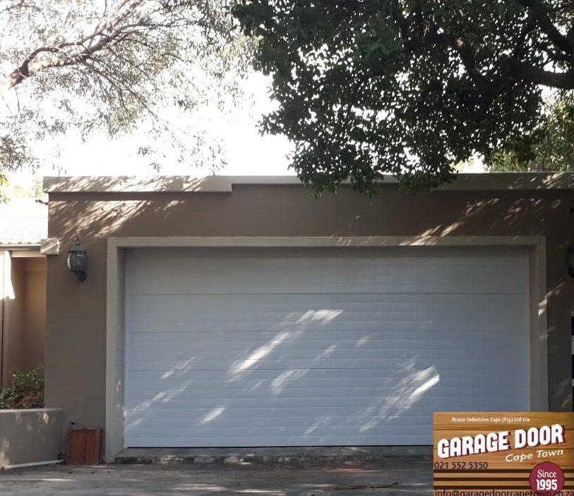 White garage door on a tan building, under tree branches.