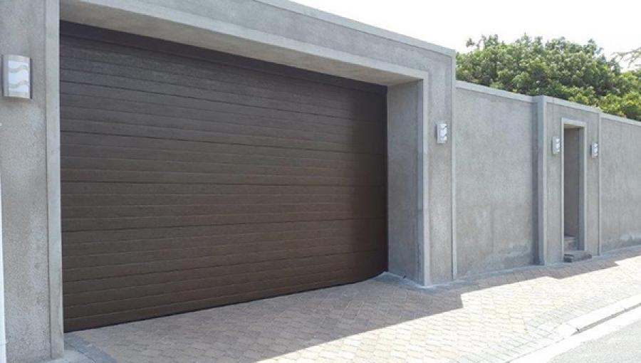 Brown garage door in a concrete frame, part of a gray walled property.