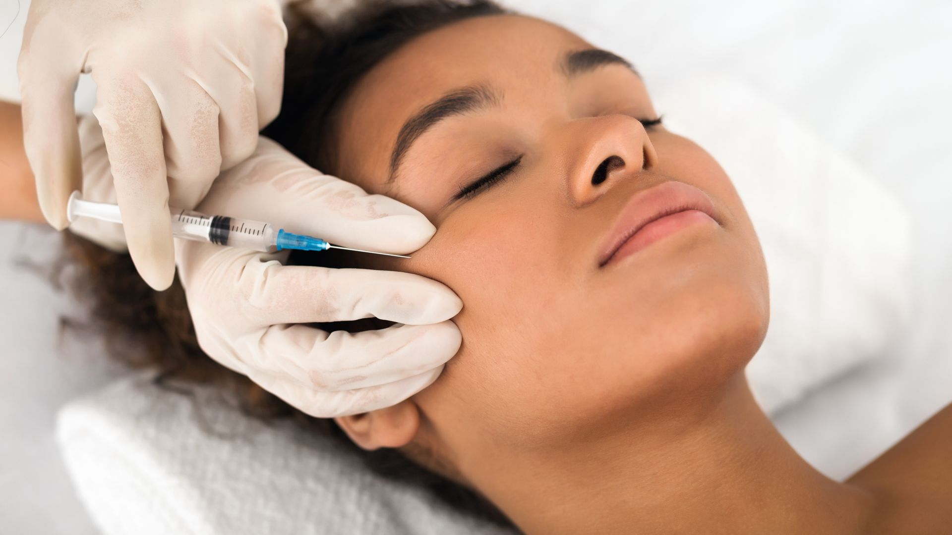 Person receiving injection near eye from gloved hand.