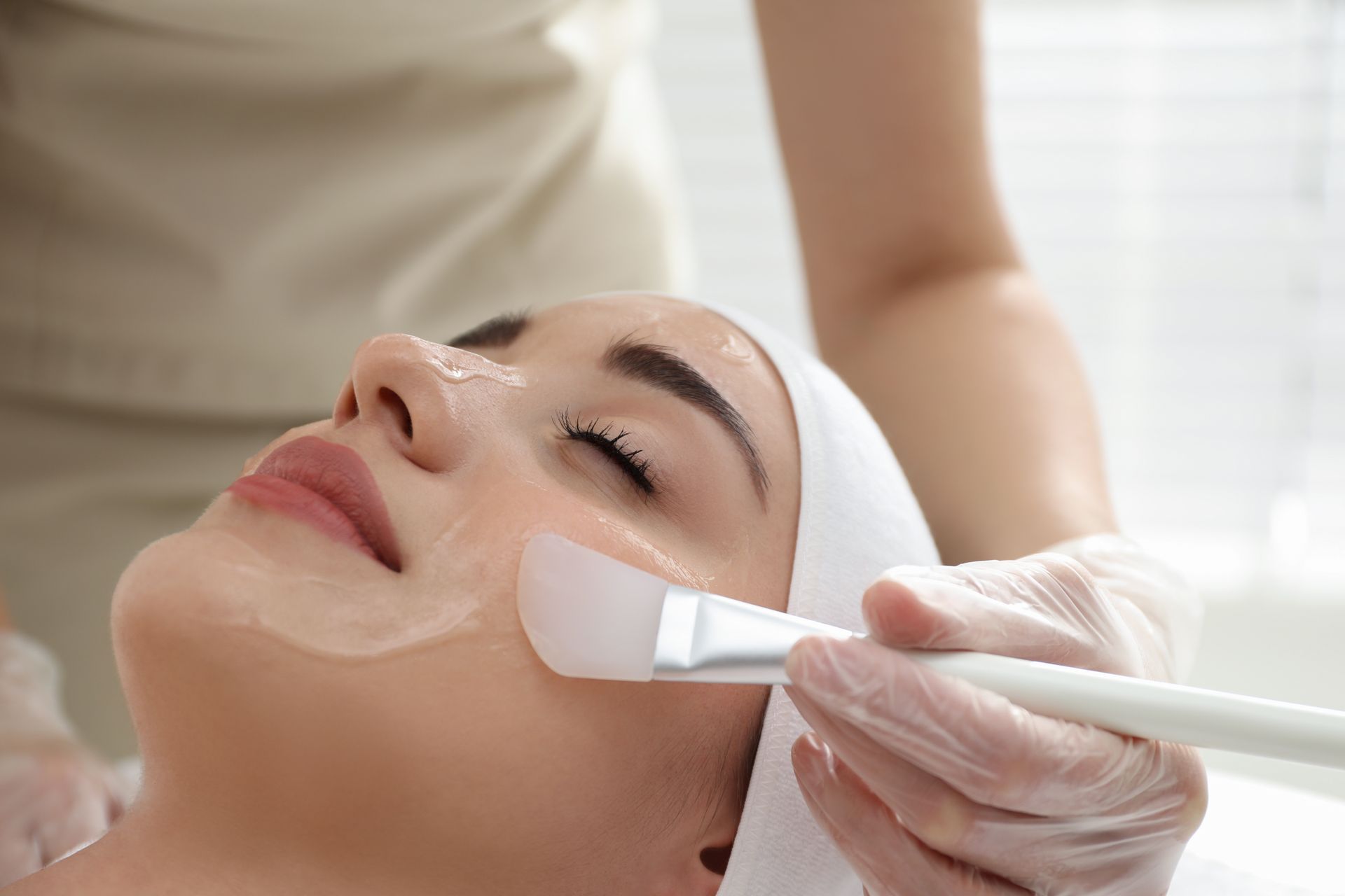 A person receiving a facial chemical peel treatment. A professional applies a product with a brush to the face.