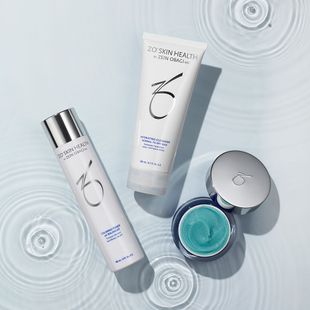 White skincare bottles and a jar with teal cream on a pale rippled background.