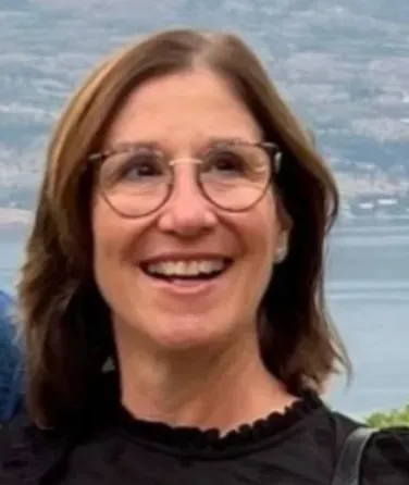 Smiling woman with glasses in front of a blurred blue water background
