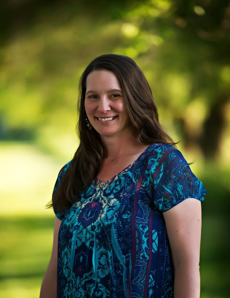 Smiling woman in a blue patterned blouse standing outdoors with a blurred green background