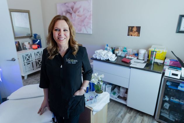 Woman standing in a treatment room beside a white exam table and skincare products on a counter