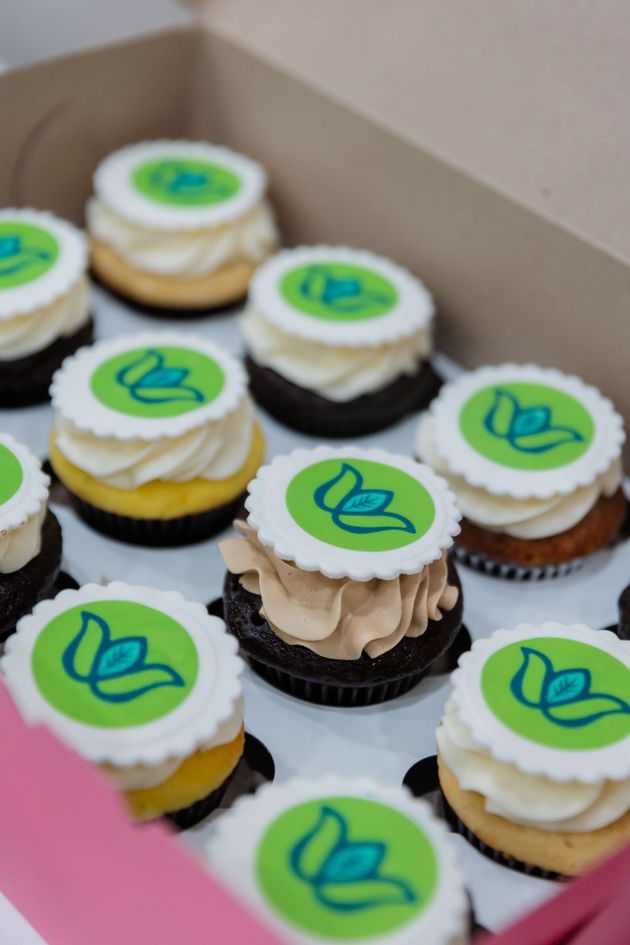 Box of assorted cupcakes with white toppers featuring a green leaf logo