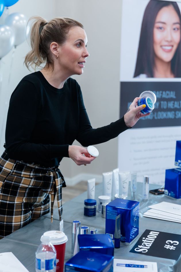 Woman presenting a blue product sample at a booth with display tables and posters behind her