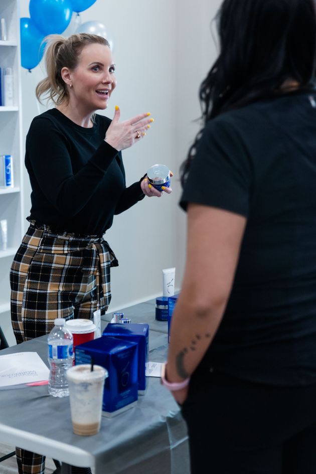 Two women talking at a table with skincare products in a bright room