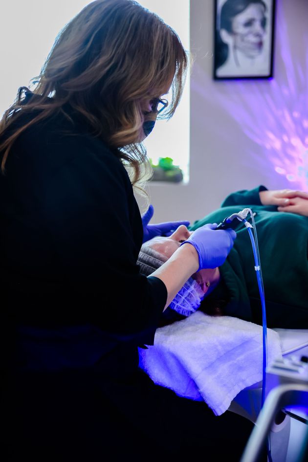 Healthcare worker wearing purple gloves performing a treatment on a seated patient in a clinic room