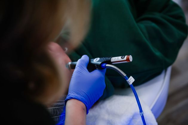 Gloved hands handling a blue breathing tube attached to a small device in a clinical setting
