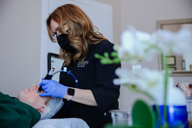 Dentist in black gloves using a device on a patient’s face in a clinic, with flowers blurred in foreground