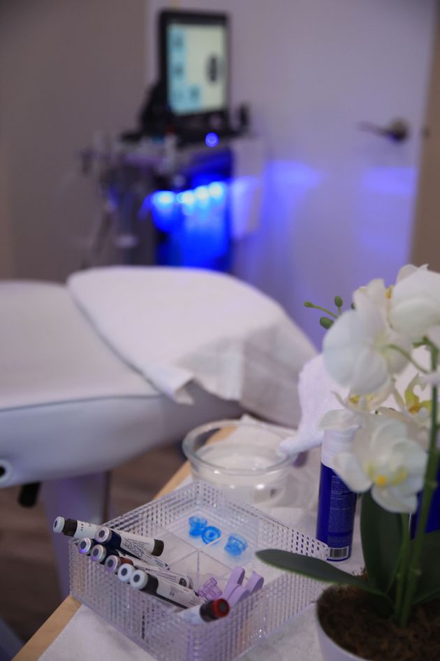 Spa treatment room with massage table, blue-lit equipment, and white flowers in foreground