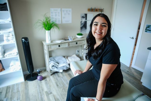 Smiling woman seated on a chair in a bright home office with a desk, plant, and open shelves.