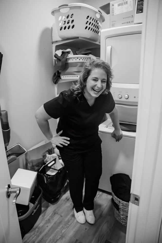 Woman smiling in a narrow laundry closet beside a stacked washer and dryer, with storage baskets above.