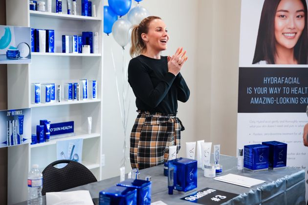 Woman clapping beside a table of blue products at a promotional booth with shelves and balloons behind her