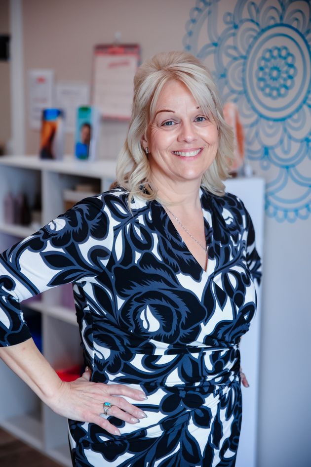 Smiling woman in black-and-white dress standing with hand on hip in a patterned office setting