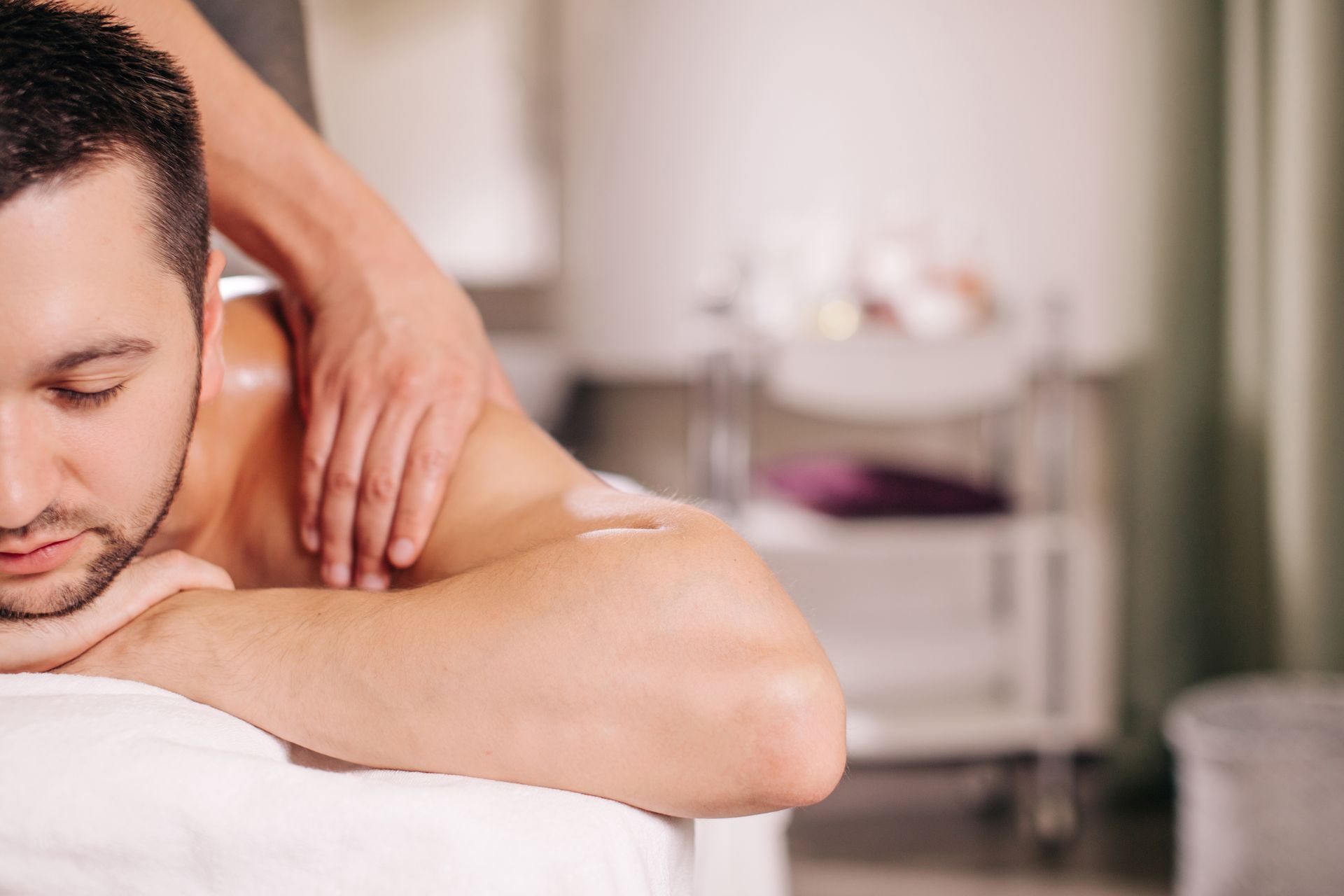 Man receiving a shoulder massage in a spa, with a blurred treatment table in the background
