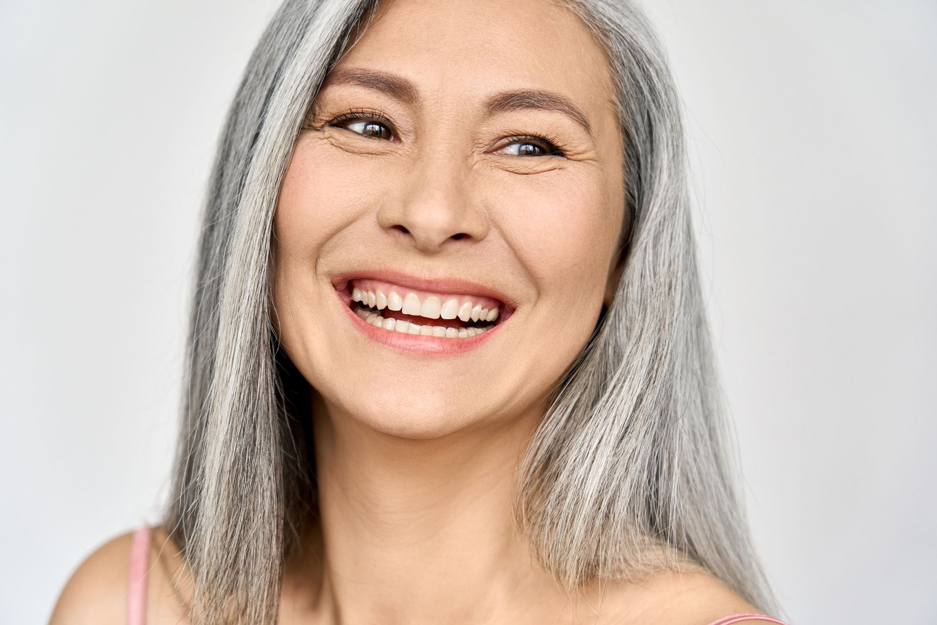 Smiling older Asian woman with long, silver hair against a white background.