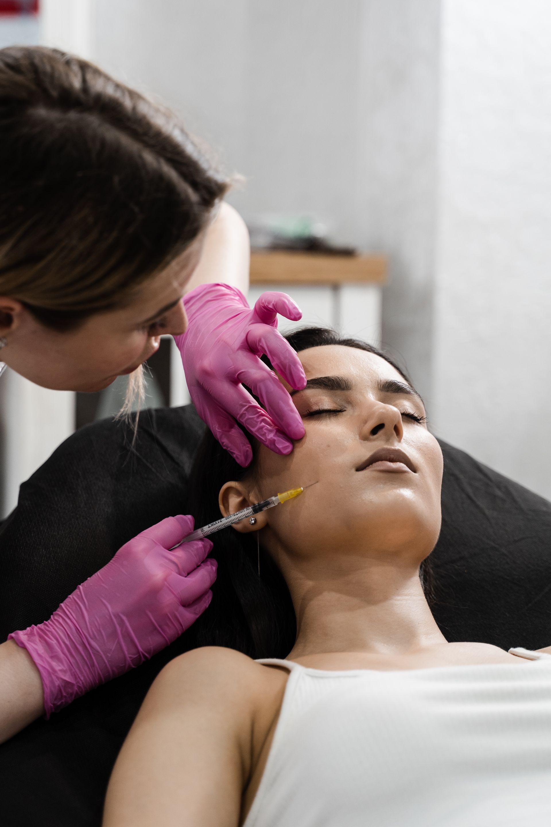 Person receiving a facial injection; a professional in pink gloves performs procedure.