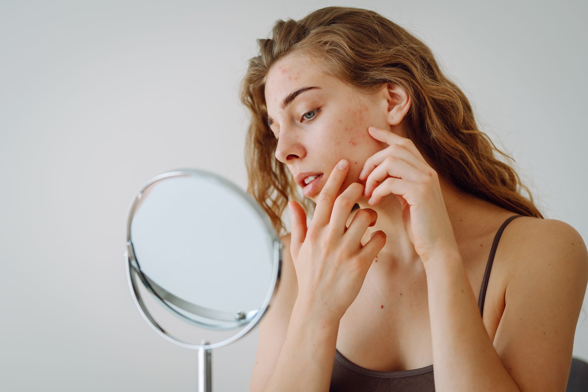 A woman is looking at her face in a mirror.