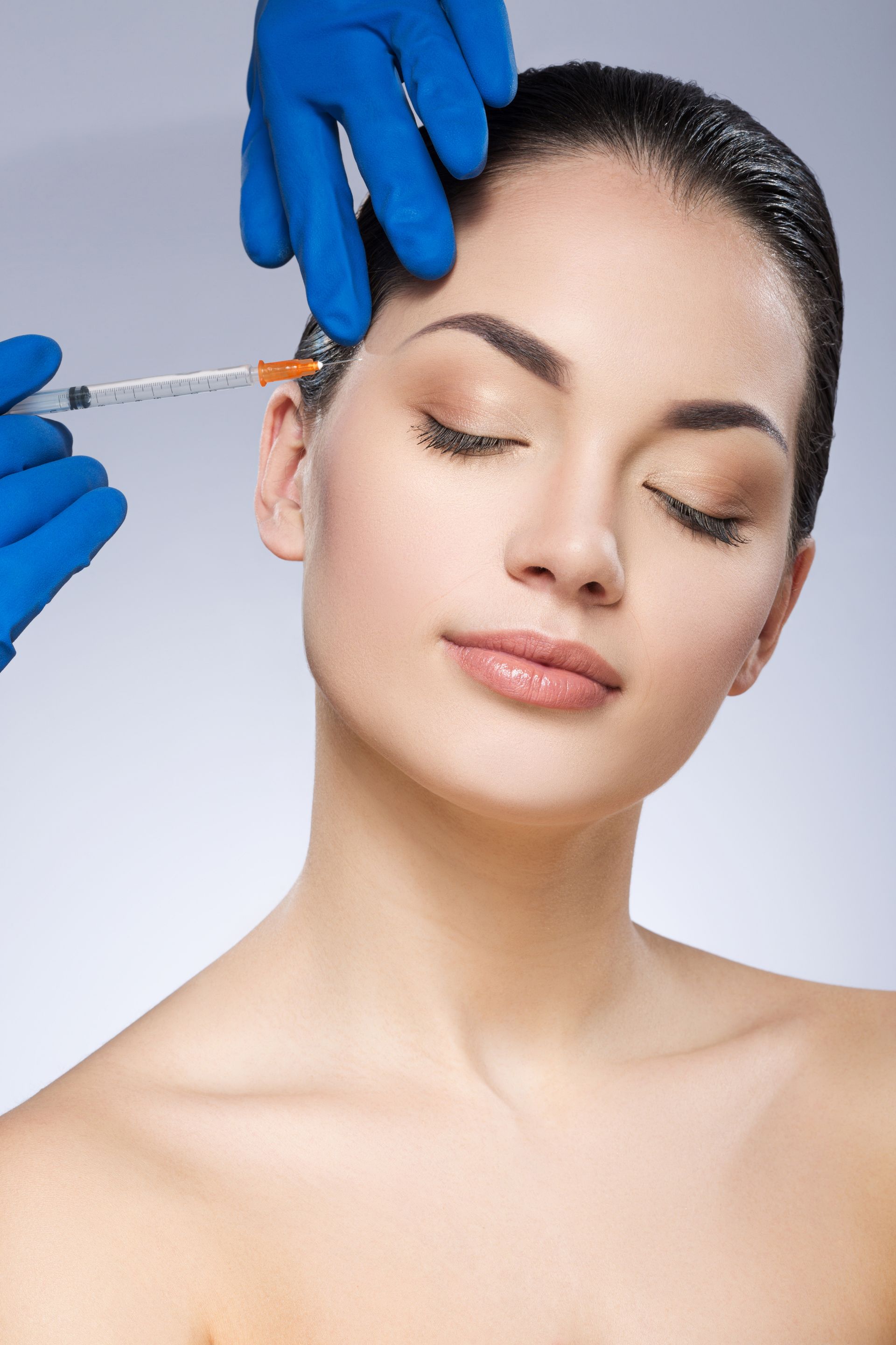 Person receiving injection in the forehead; hands in blue gloves hold syringe.