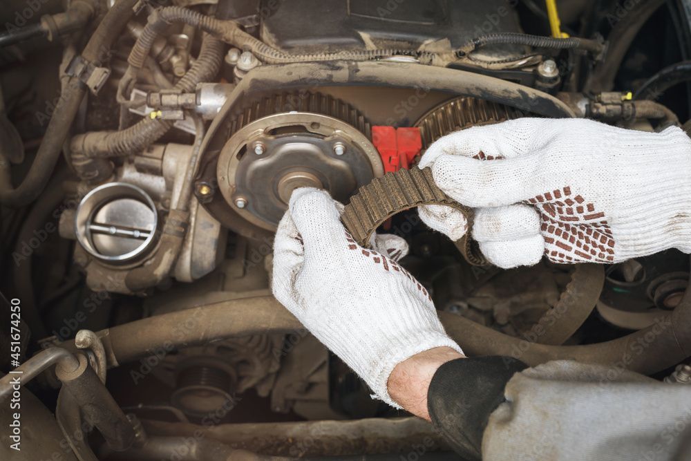 Mechanic kneeling beside a silver car, tightening the front wheel in a garage.