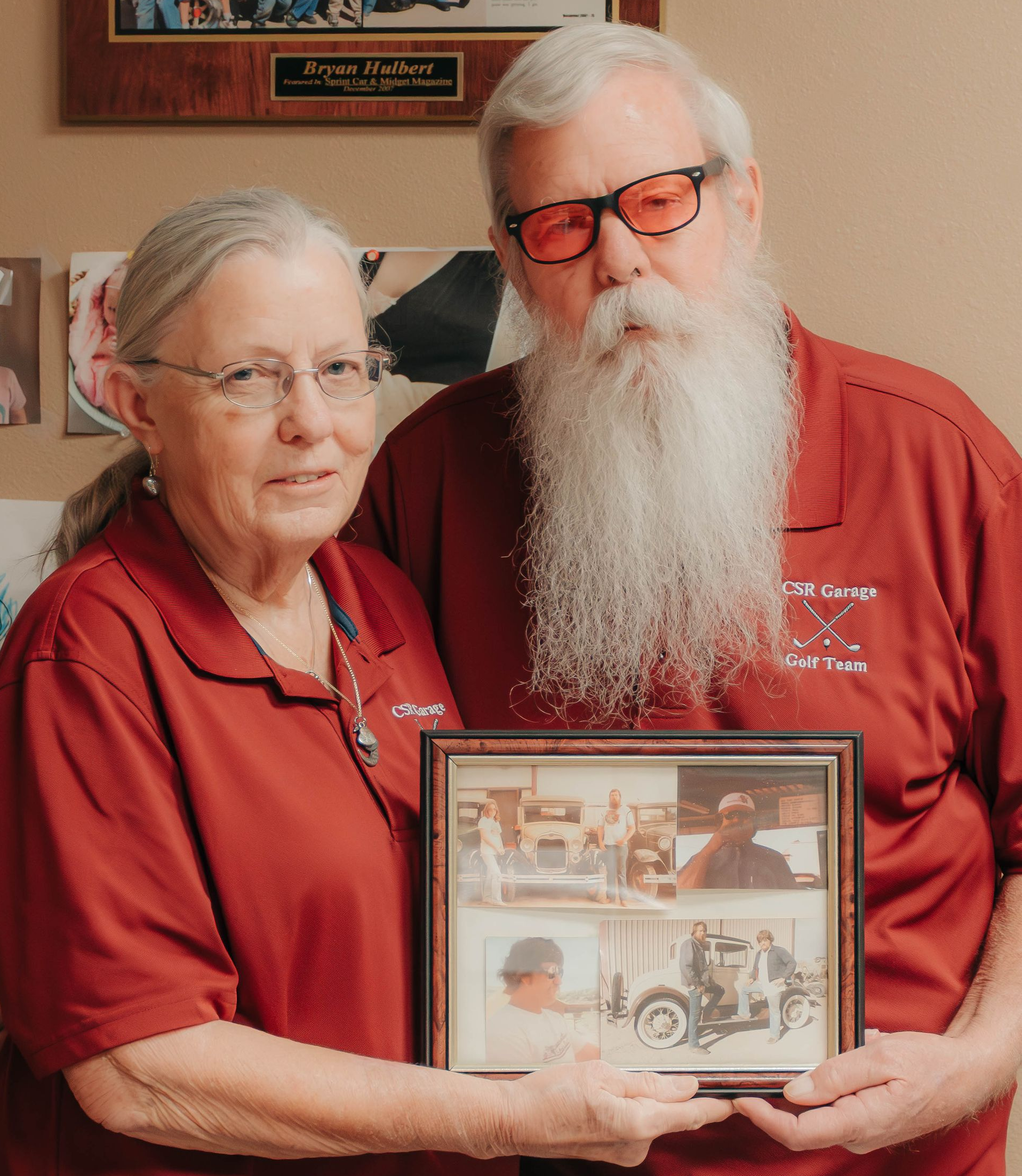 Two people in red shirts holding a framed collage, standing indoors.