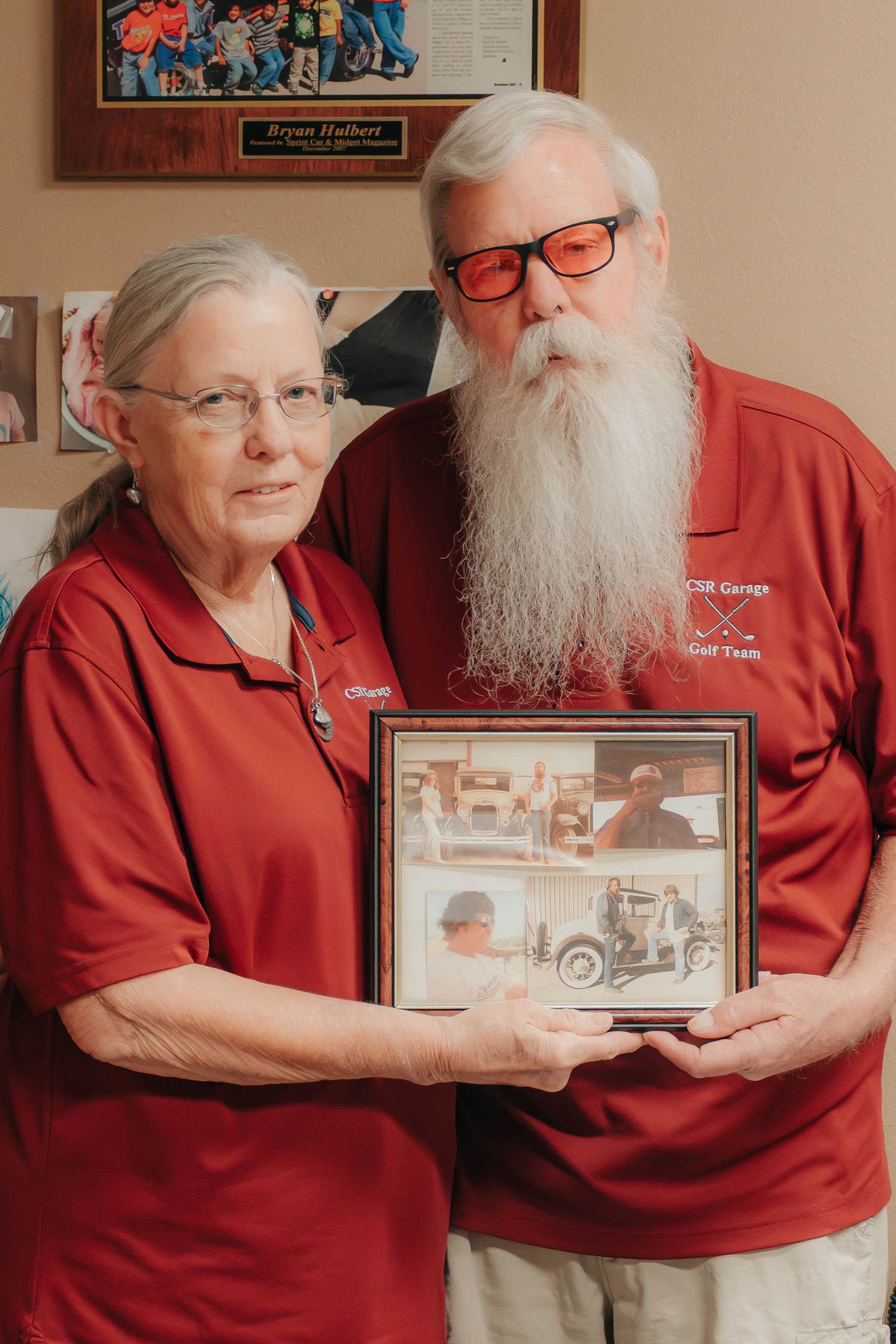 Two people in red shirts holding a framed photo indoors