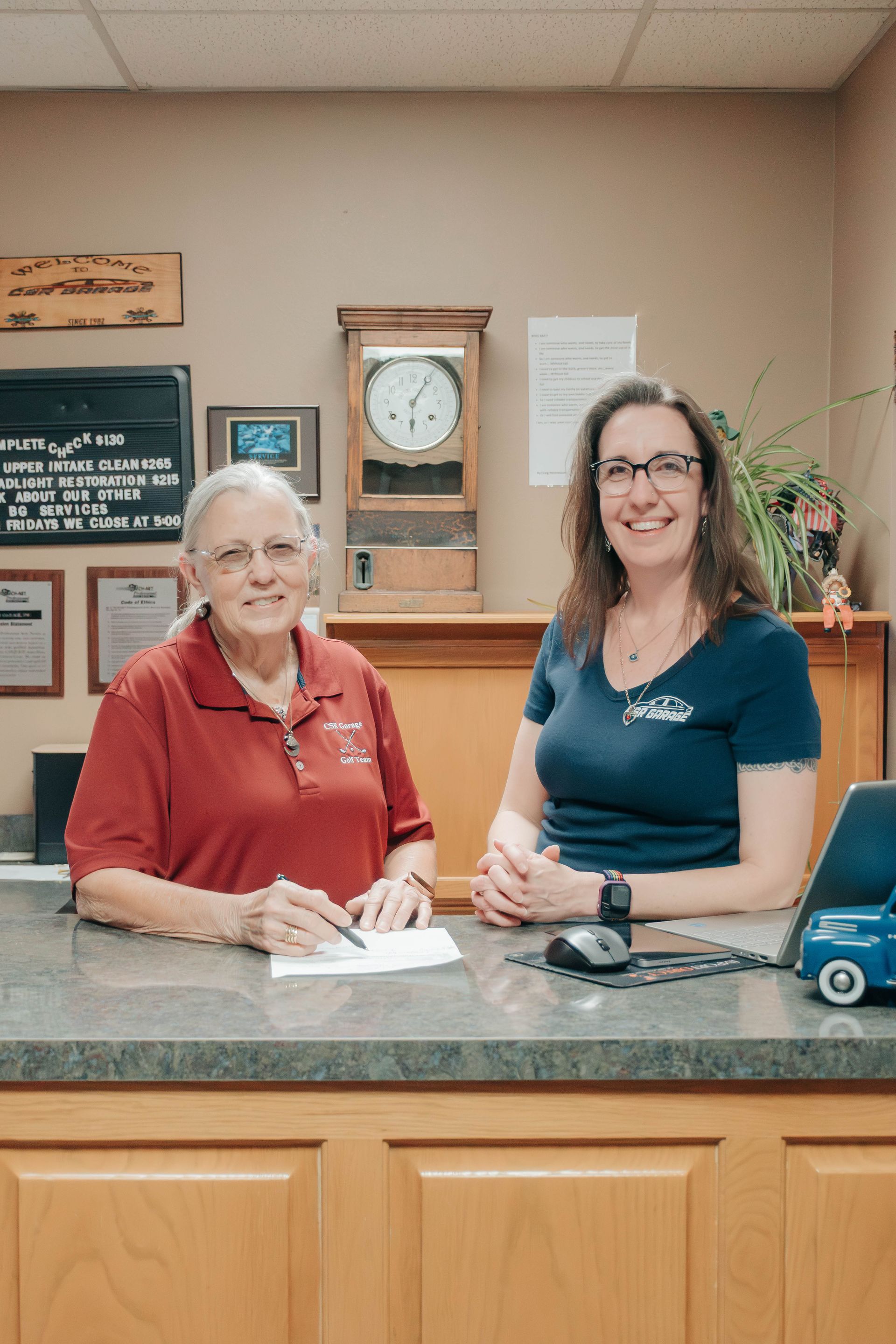 Two women standing behind a front desk in a reception area, smiling at the camera.
