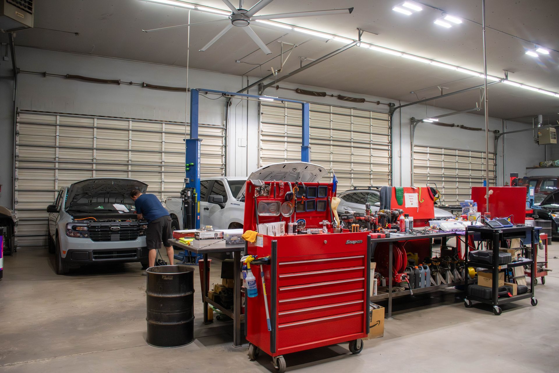 Auto repair garage with red tool cabinets, a black SUV, and a mechanic working inside a spacious workshop