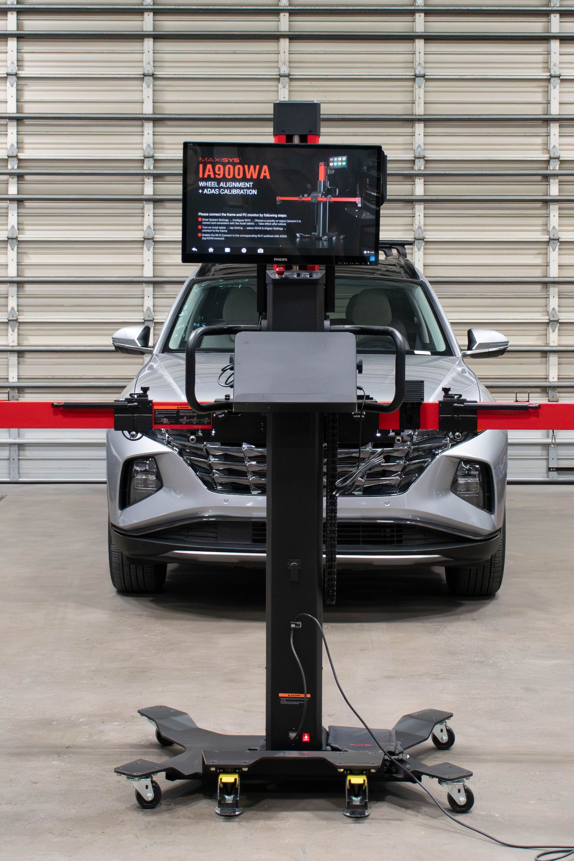 Mobile sensor rig in front of a parked SUV inside a warehouse, with monitor on a wheeled stand