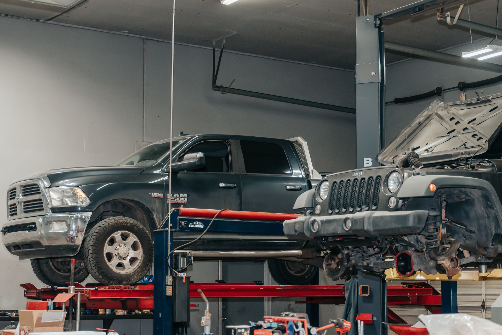 Two vehicles on lifts in an auto repair shop, including a black pickup and a Jeep under service.
