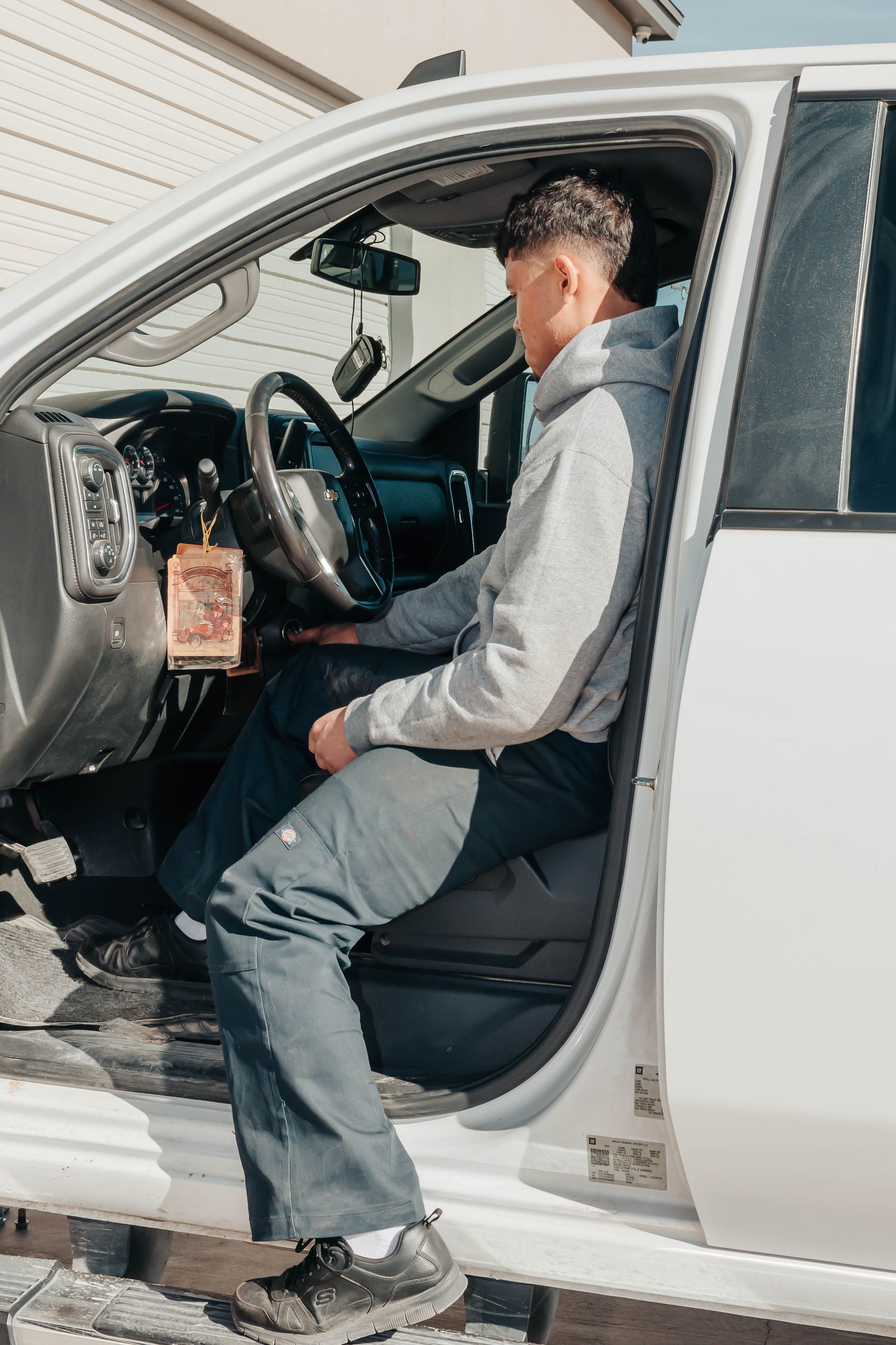 Person sitting in a white car with the driver’s door open, looking toward the steering wheel