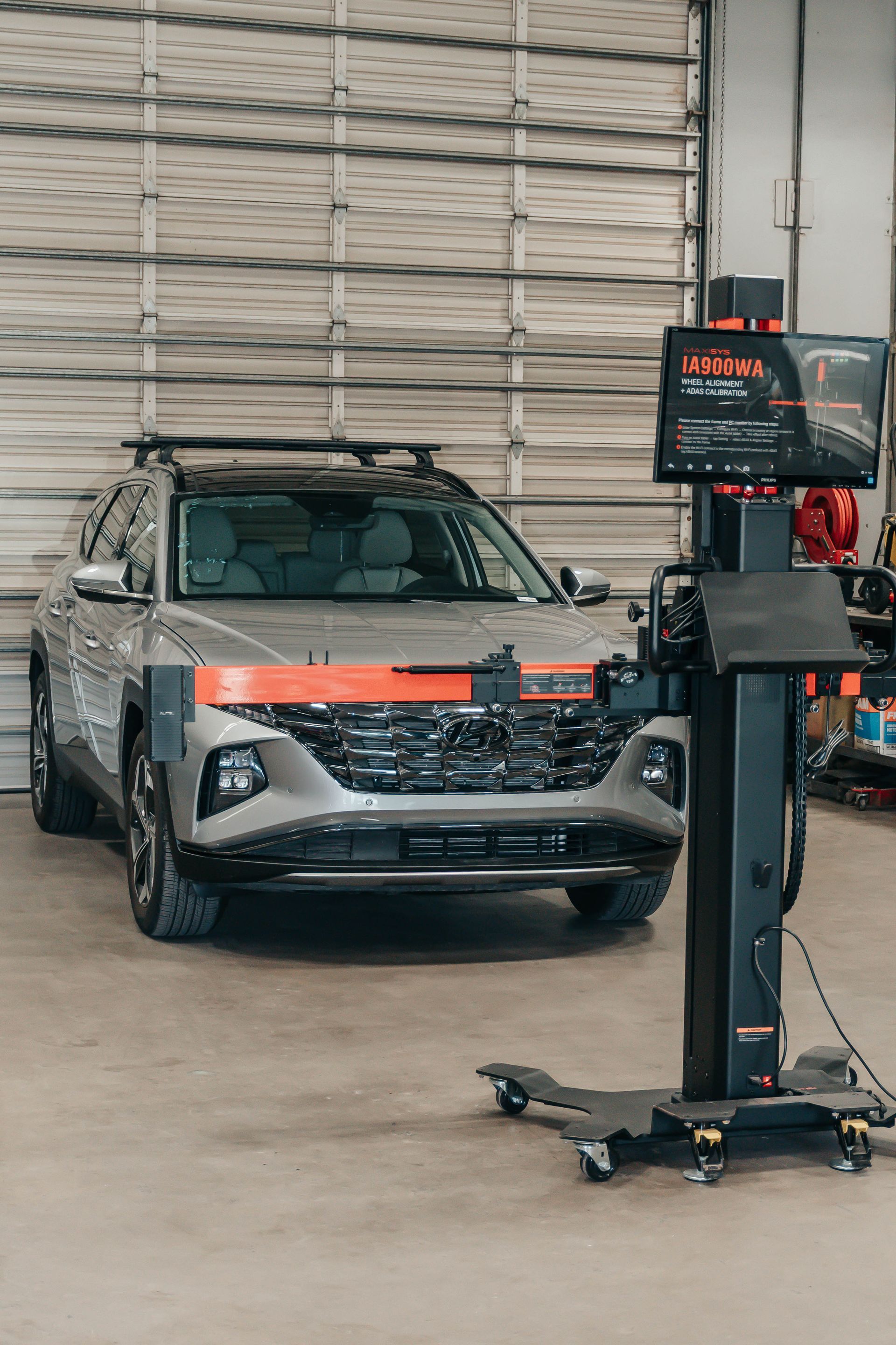 Silver car in a workshop, positioned on a vehicle lift with a diagnostic stand in front.
