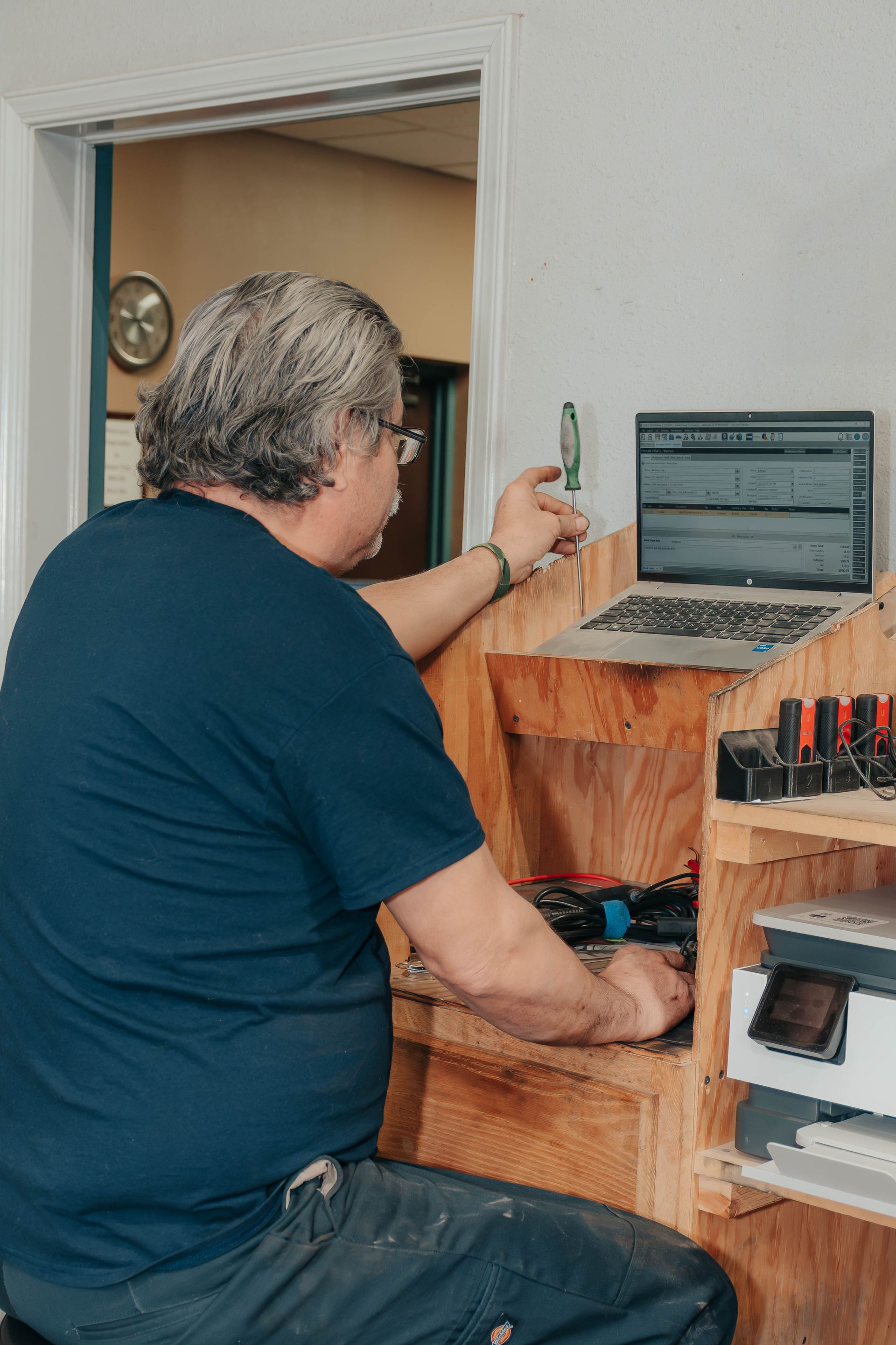 Person working at a laptop on a small wooden desk in a doorway.