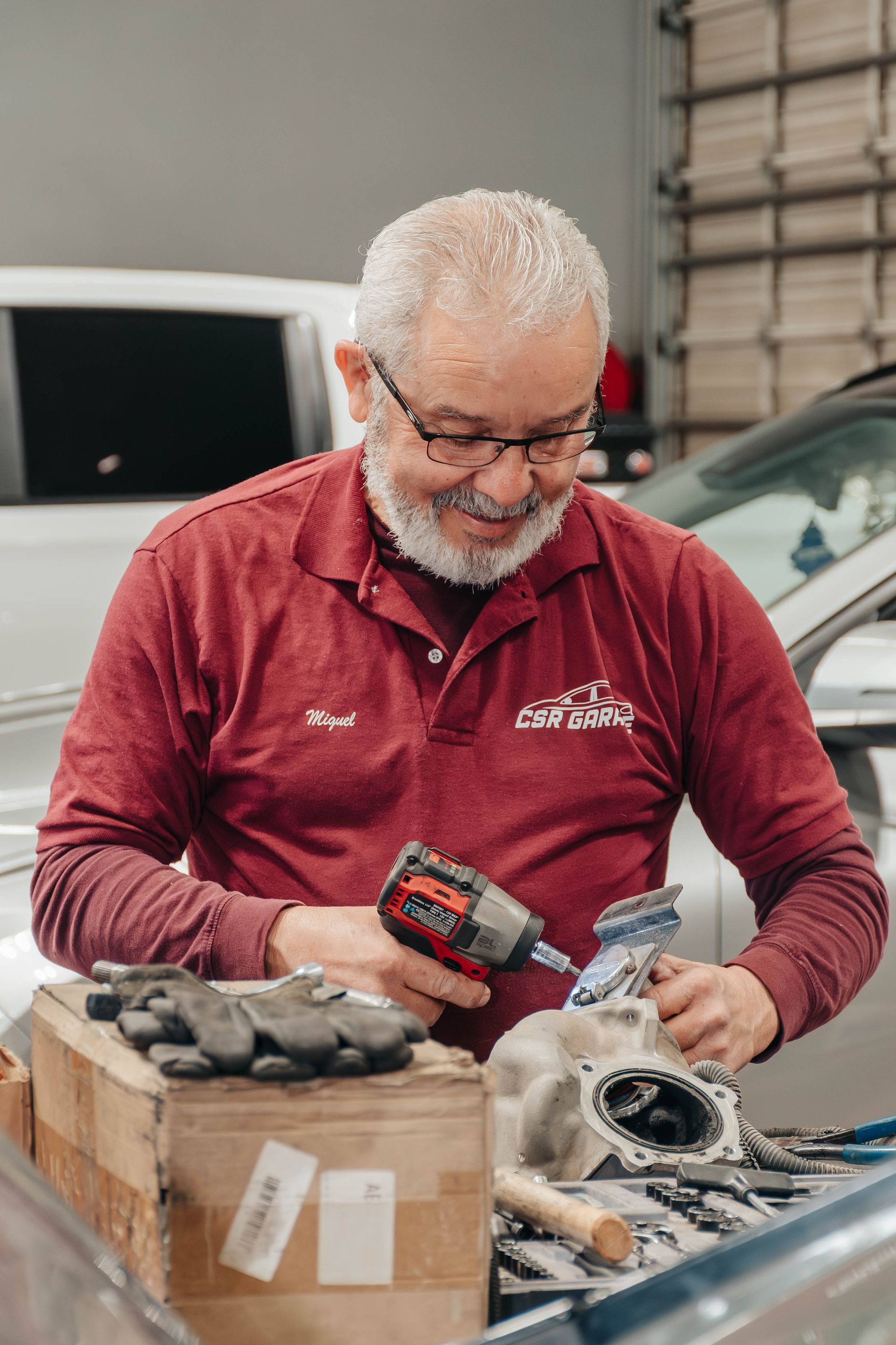 Mechanic in red shirt inspecting car parts with a handheld tool in a garage