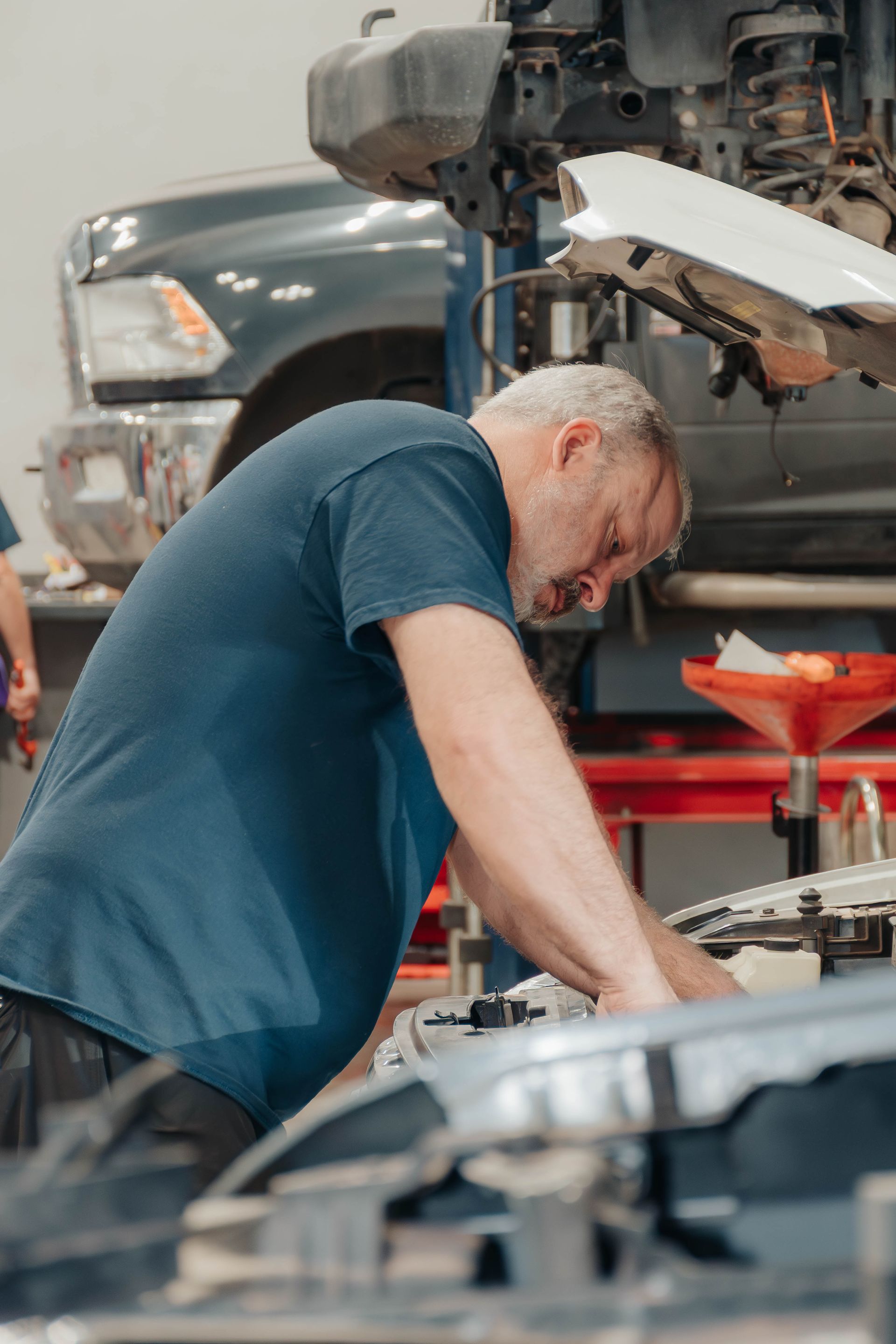 Mechanic in blue shirt working under a raised car in an auto repair shop
