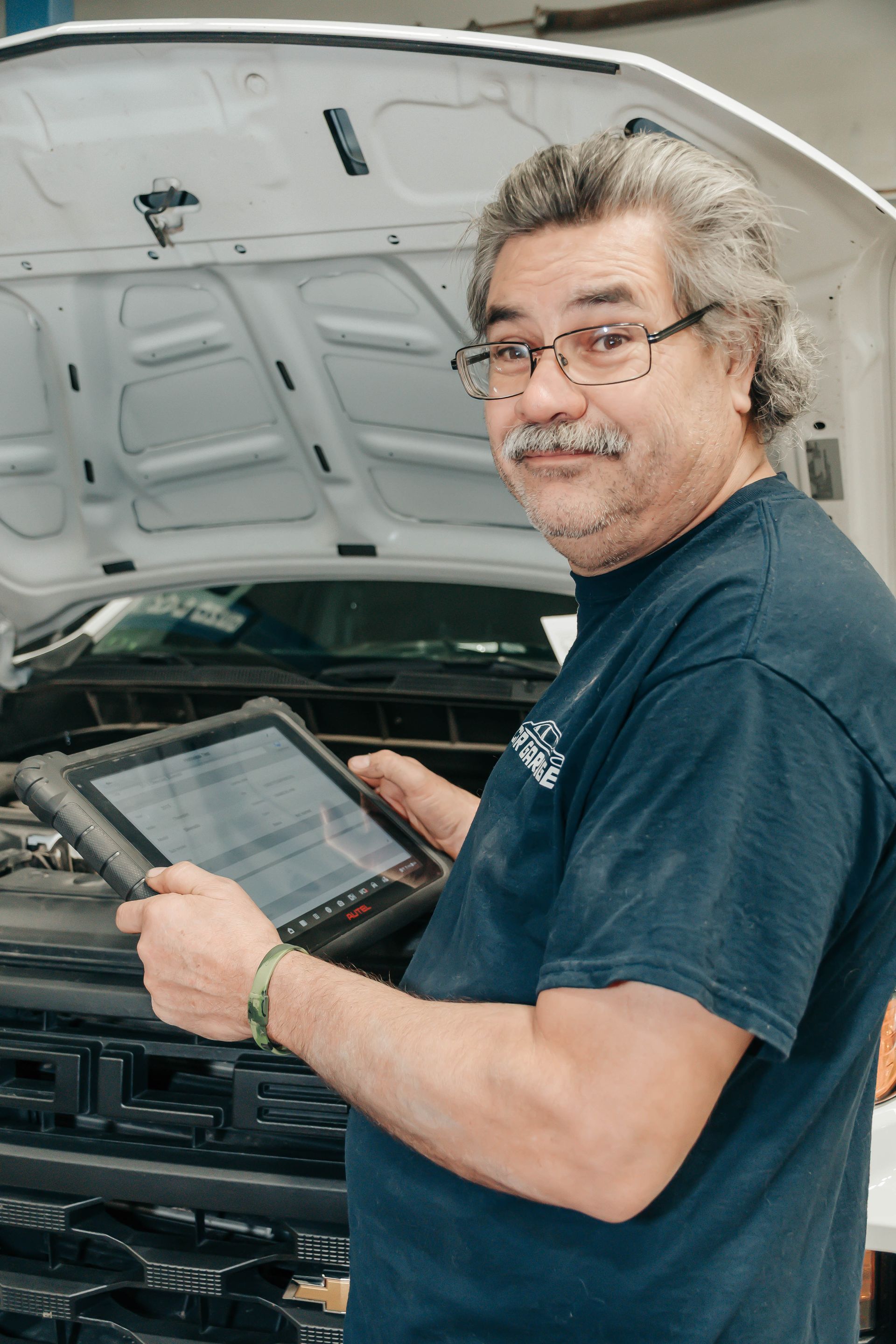 Man holding a tablet while working in front of an open car hood in a garage