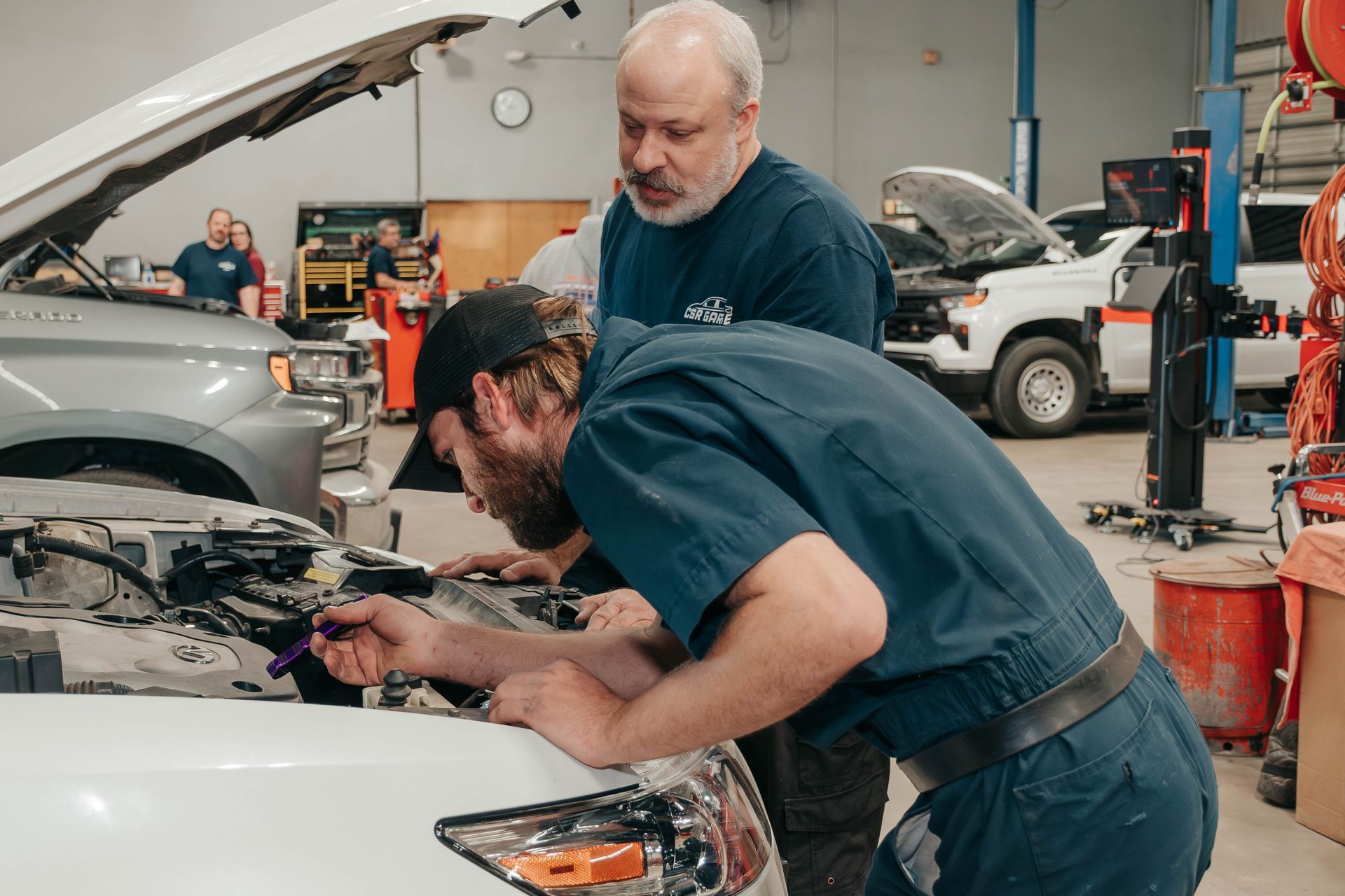 Mechanic working under an open car hood, inspecting engine components in a garage