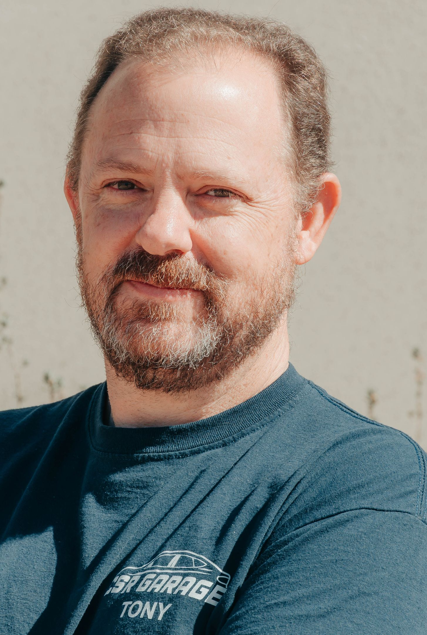 Portrait of a man with short hair and a beard, wearing a blue T-shirt against a plain wall.
