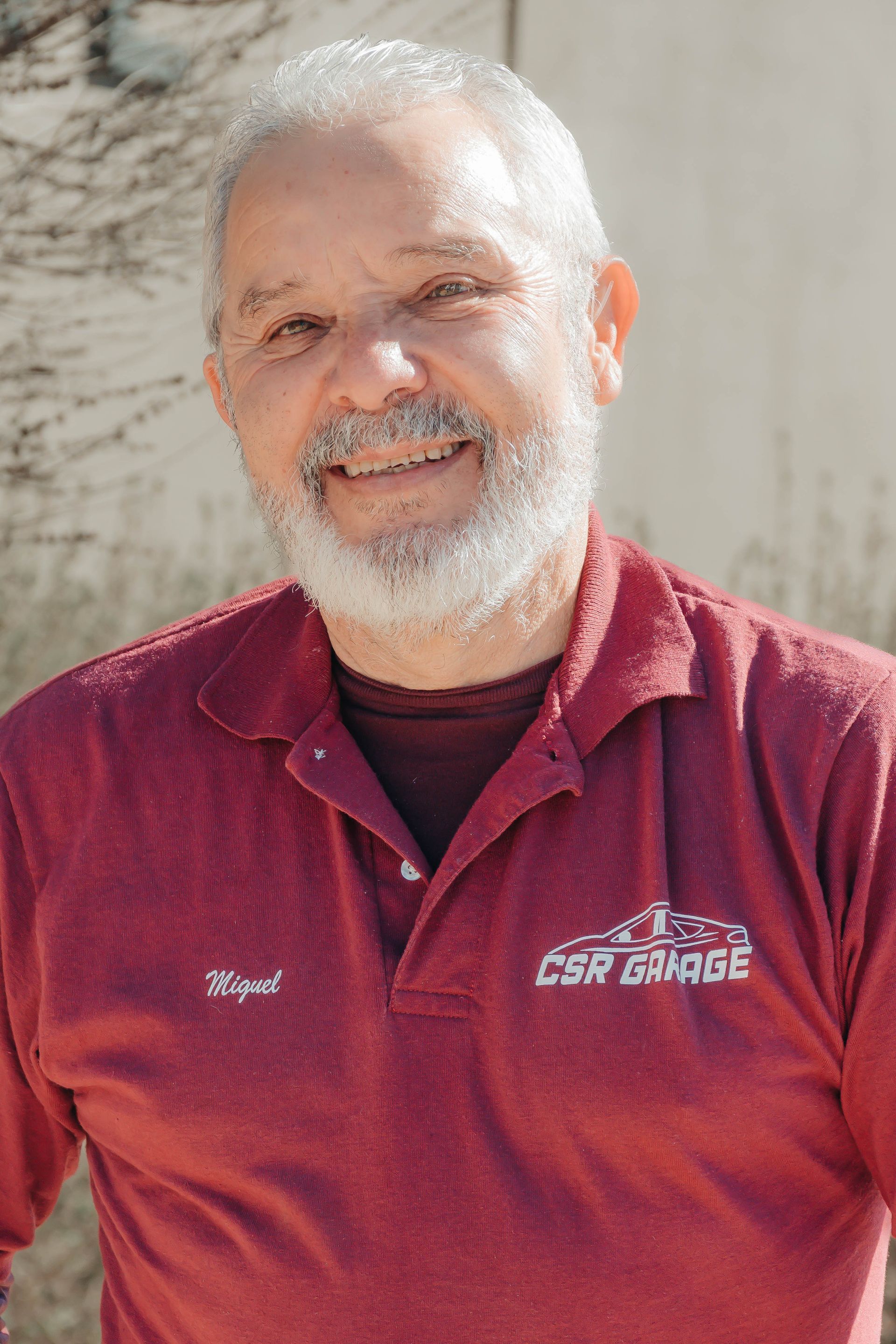 Smiling man in a maroon polo shirt standing outdoors against a light wall