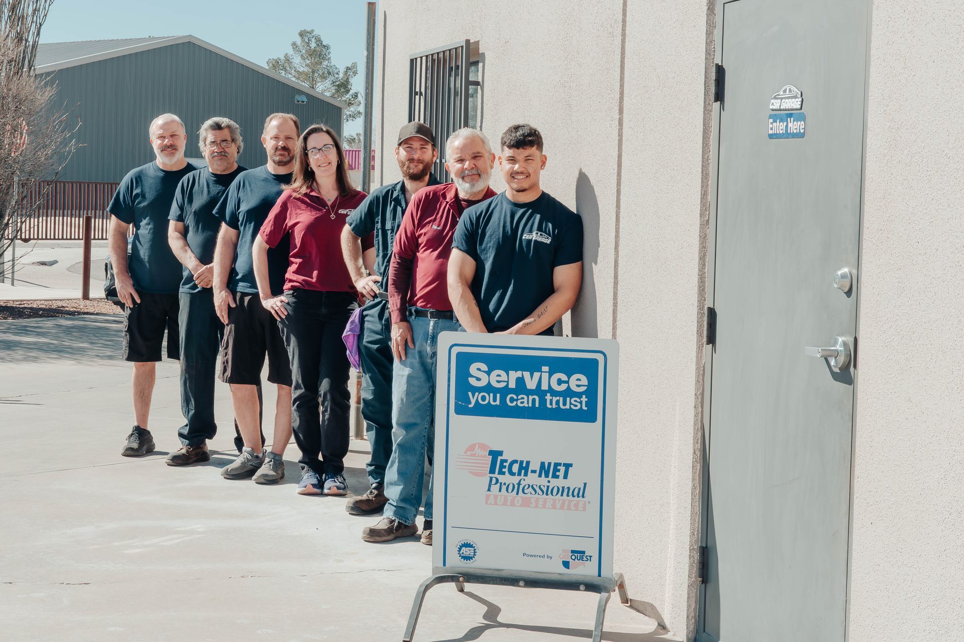 Group of people standing outside a building beside a blue service sign on a sidewalk